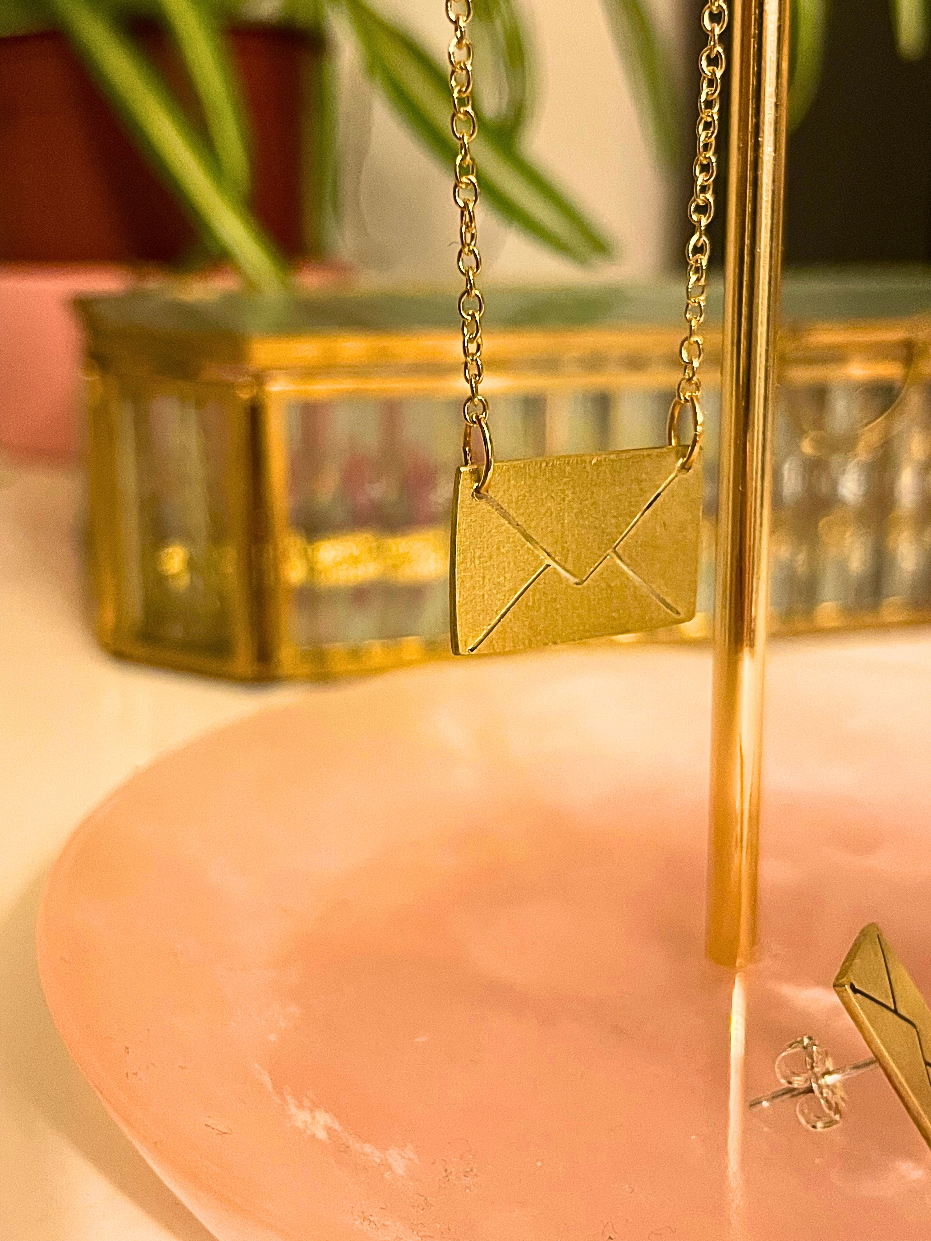 Gold envelope-shaped pendant on a chain against a blurred background
