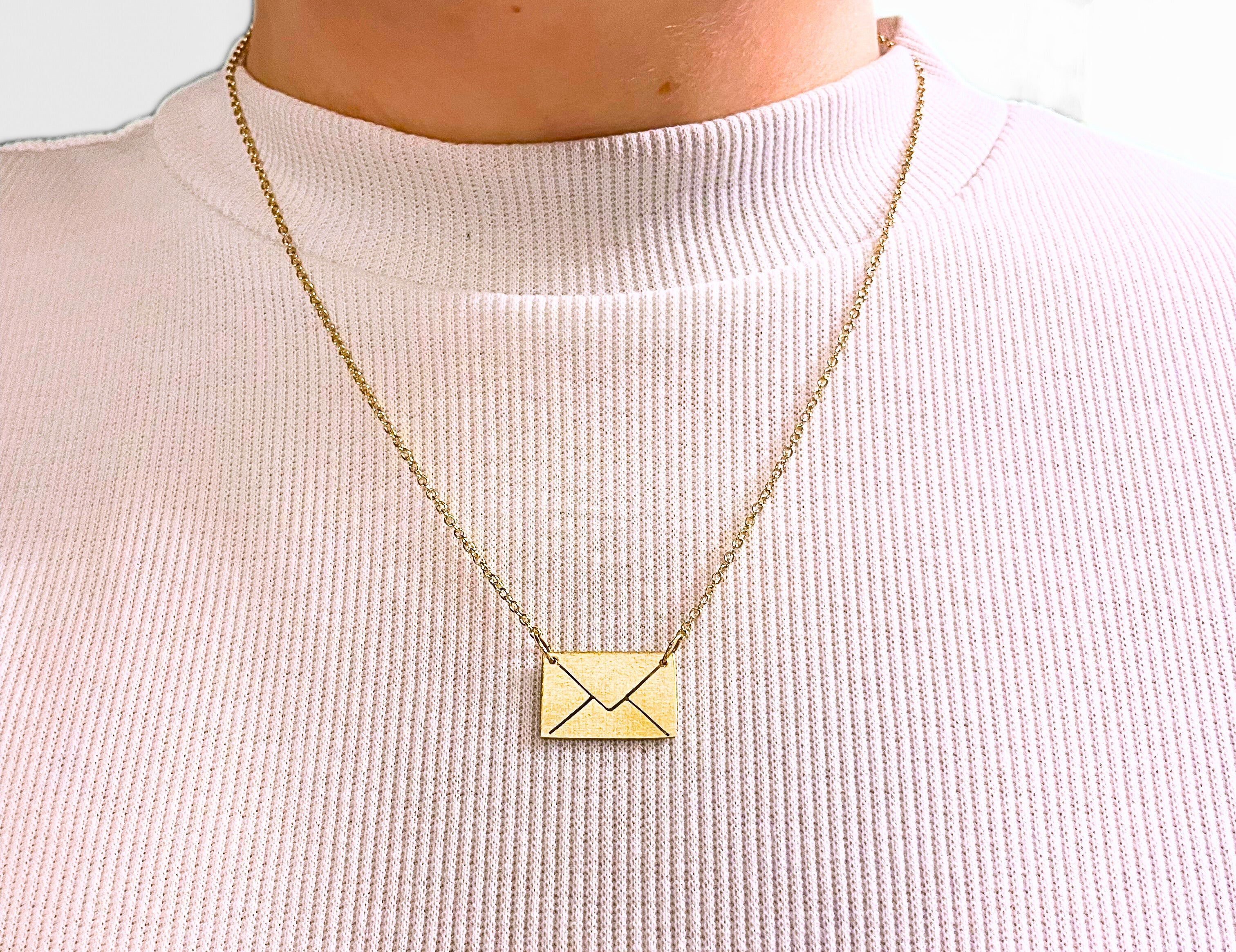 Gold necklace with a square pendant on a light pink sweater