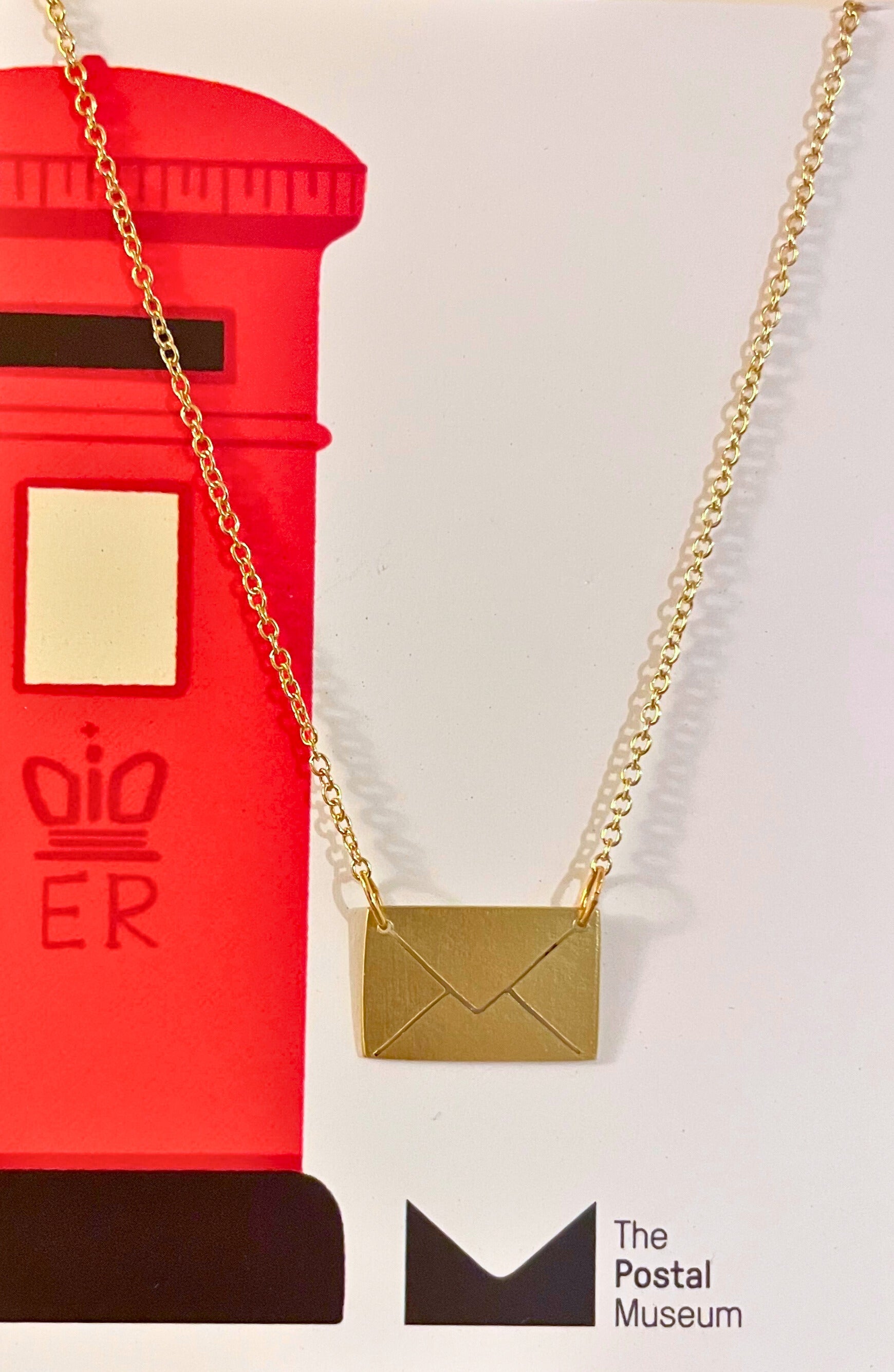 Gold necklace with a pendant shaped like an envelope in front of a red postbox, with &