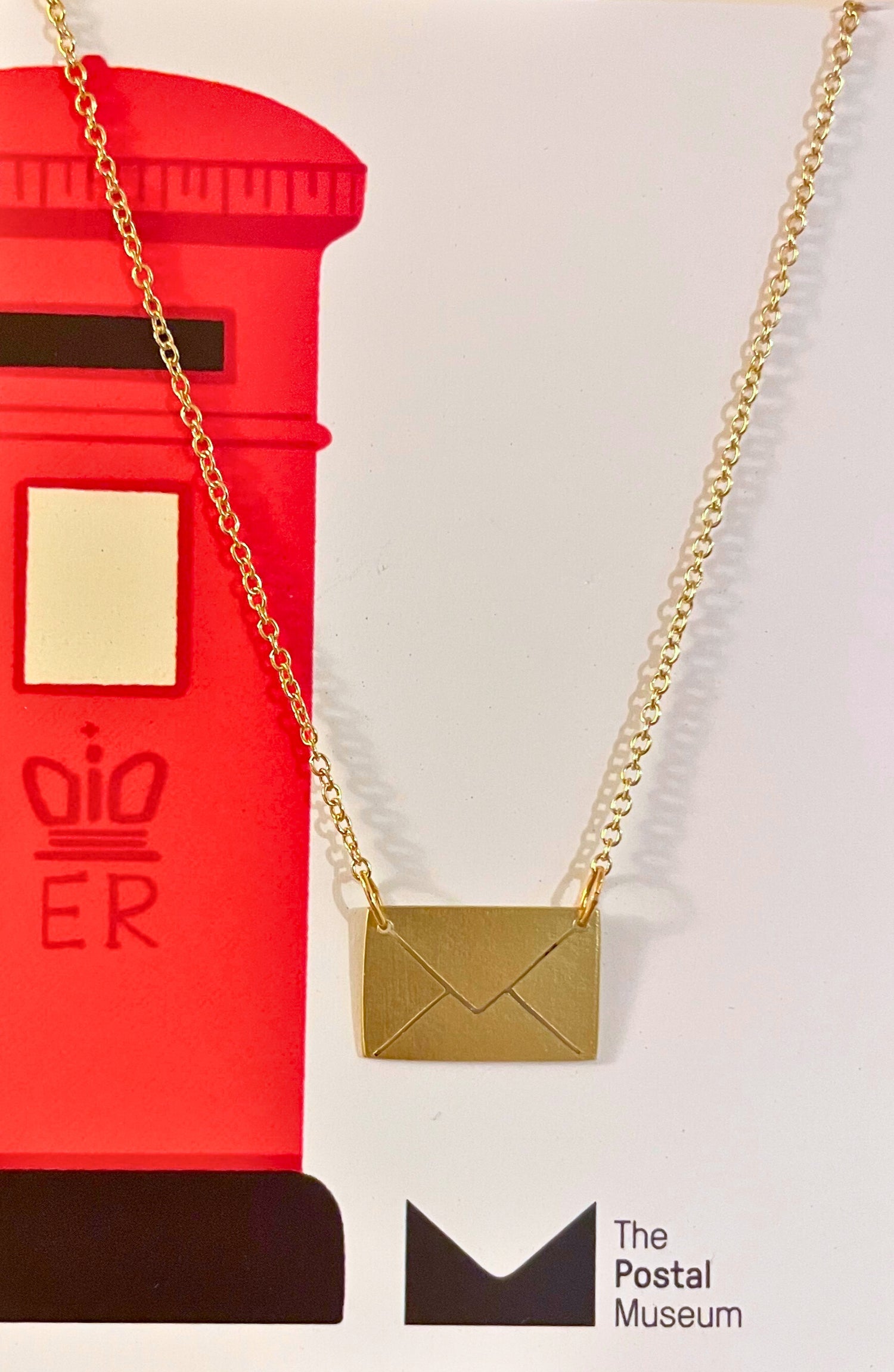 Gold necklace with a pendant shaped like an envelope in front of a red postbox, with &