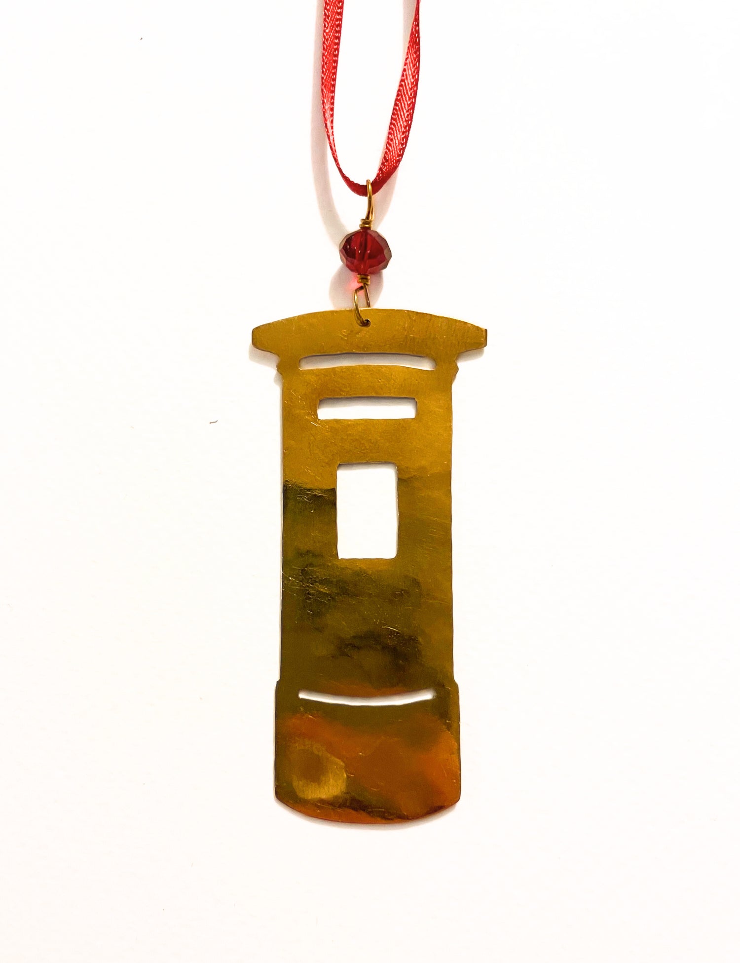Brass pendant on a red string against a white background